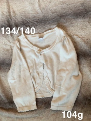 Vit bolero med volangkant - Söt vit bolero med volangkant längs halsringning, ärmslut och nederkant. Boleron har en knapp framtill Passar perfekt till lager på lager och ger en gullig touch till outfiten.🌸Fint använt skick. Storlek 134/140