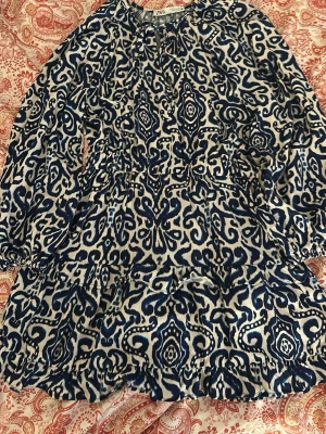 Blåvit mönstrad kortklänning Zara - Kortklänning från Zara i blått och vitt med unikt mönster. Klänningen har långa ärmar, volangdetaljer och knytning vid halsen. Perfekt för dig som gillar boho-vibbar och vill sticka ut med en cool printad look.