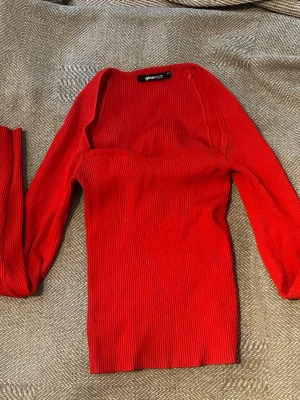 Röd ribbad topp från Gina Tricot - Trendig röd långärmad topp från Gina Tricot i ribbad kvalitet. Toppen har en snygg fyrkantig urringning och figurnära passform som framhäver siluetten. Perfekt att styla med jeans eller kjol för en cool look.