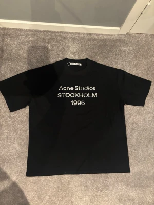 Svart Acne Studios t-shirt Stockholm - Snygg svart t-shirt från Acne Studio. Perfekt för dig som gillar stilrena och ikoniska plagg från populära märken. Storleken är S men sitter mycket större än vad jag trodde så jag skulle säga att det passar mer för M eller L om man inte gillar lite oversized fits