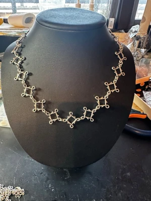 Silvrigt handgjort halsband i metall - Unikt halsband i silverfärgad metall med handgjorda länkar som bildar ett geometriskt mönster. Halsbandet har en modern och edgy vibe med sina fyrkantiga former och öppna öglor. Perfekt för dig som gillar statement-smycken och vill sticka ut.