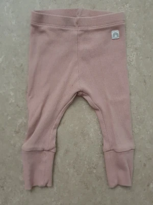 Leggings - Supersöta ljusrosa leggings i ribbad bomull med breda muddar vid bensluten. De har en liten patch med regnbågsmotiv vid midjan och är perfekta för en chill och bekväm stil. Passar till allt och är riktigt mjuka och stretchiga.