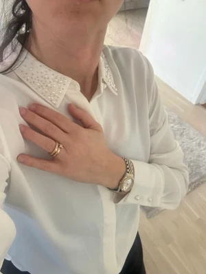 Vit blus med pärlkrage - Stilren vit blus med lång ärm och klassisk krage dekorerad med små pärlor. Blusen har knäppning framtill och är tillverkad i ett lätt, något transparent tyg som ger en elegant känsla. Perfekt för dig som gillar detaljer och vill ha en chic look.
