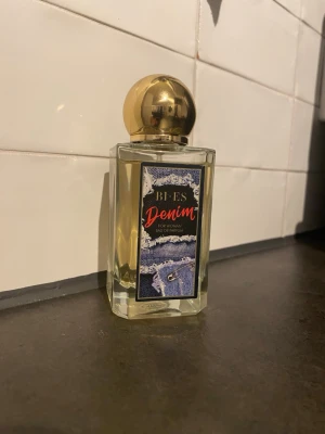 BI-ES Denim Eau de Parfum - BI-ES Denim Eau de Parfum för kvinnor med en cool etikett i denimstil. Flaskan är rektangulär i genomskinligt glas med en rund, guldig kork. Perfekt för dig som gillar trendiga och snygga detaljer på parfymflaskan.