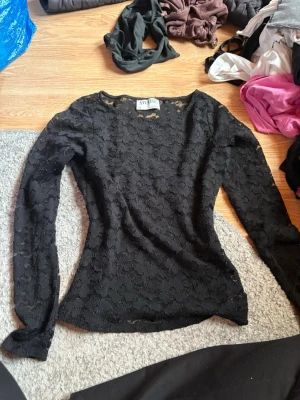 Svart spetsblus från AWARE - Säljer en svart långärmad spetsblus från AWARE. Blusen har ett genombrutet spetsmönster och är figurnära i modellen. Nypris 500 men säljer billigare pga hålet på sidan men de syns knappt