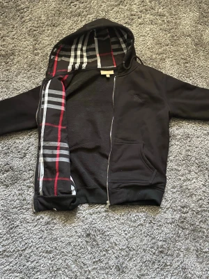 Burberry zip up hoodie - Burberry hoodie säljes. Använd några gånger men i väldigt fint skick, inga fläckar eller skador. Klassisk Burberry-rutig detalj på insidan.  Storlek: S Pris: 650 (kan diskuteras)  Frakt betalas av köparen eller möts upp i Östersund 