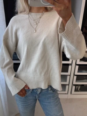 Beige stickad tröja - Mysig beige stickad tröja och bred ribbad kant nedtill samt vid ärmslut. Tröjan har rund halsringning och är tillverkad i ett mjukt material som passar perfekt till jeans. Enkel och stilren design utan synligt märke.