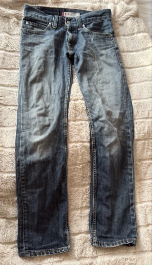 Levis 511 - Säljer ett par blå jeans med rak passform och snyggt tvättad look. Jeansen har klassiska sömmar och subtila slitningar för en avslappnad stil. Perfekta till vardags och passar till det mesta. 