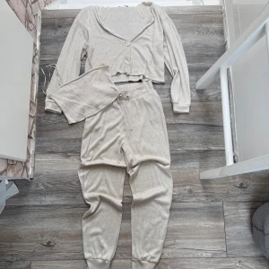 Beige loungewear-set - Mysigt beige loungewear-set med croppad topp, en långärmad kofta till med knappar. Tillhörande byxor med dragsko i midjan och muddar vid benen. Perfekt för chill dagar hemma.