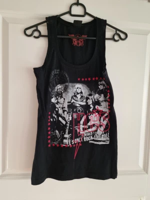 Svart linnetopp med rockmotiv - Cool svart linnetopp från Hot Kiss med stort rockinspirerat tryck i vitt och rött framtill. Motivet har stjärnor och text, och toppen har en rund halsringning och ärmlös design. Perfekt för dig som gillar edgy och musikstil.