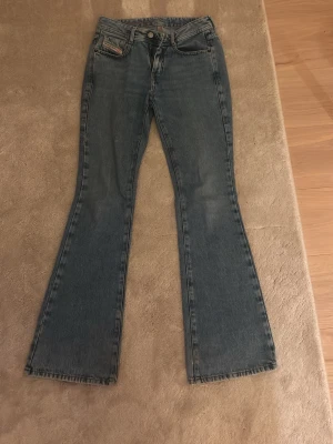 Blå bootcut jeans från diesel - Säljer ett par klassiska blå bootcut jeans från diesel.. Jeansen har fem fickor, normal midja och råa kanter längst ner på benen för en avslappnad look. Tillverkade i slitstarkt denimtyg och har en vintagekänsla med diskreta slitningar. Har ett litet hål vi skrevet men inget som syns när man har på sig de. Köptes för 2000kr i butik.