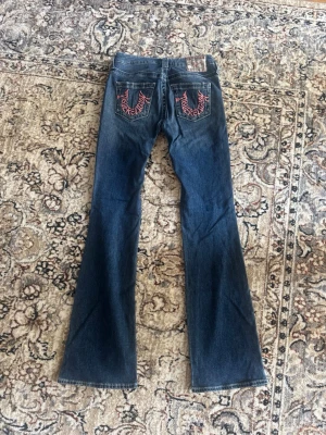 True Religion jeans - Helt nya bootcut jeans från True Religion i modellen Becca mid rise. Coola rosa detaljer på bakfickorna, Aldrig använda och därför i nyskick. Nypris var 1700kr. Köpta ifrån Nelly. Storlek 26.