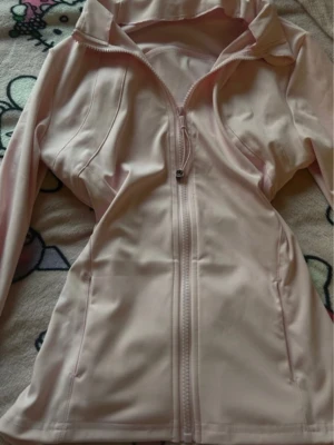 Ljusrosa define jacket med dragkedja - Snygg ljusrosa define jacket med hel dragkedja framtill. Jackan har två fickor på sidorna och är tillverkad i ett mjukt, stretchigt material som känns sportigt och bekvämt. Perfekt för träning eller chill dagar.