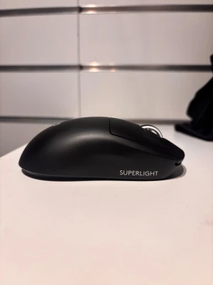 Svart Logitech Superlight mus - Säljer en svart Logitech Superlight gamingmus med slimmad och ergonomisk design. Musen har en matt yta, två sidoknappar och scrollhjul. Perfekt för dig som vill ha en lätt och snabb mus till datorn. Trådlös och stilren med diskret logotyp på ovansidan.