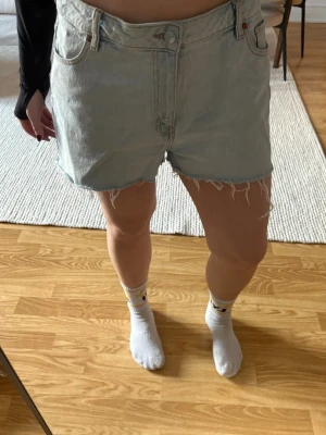 Ljusblå jeansshorts från LIA - Säljer ett par ljusblå jeansshorts från LIA med råa, fransiga benslut och klassisk femficksdesign. 