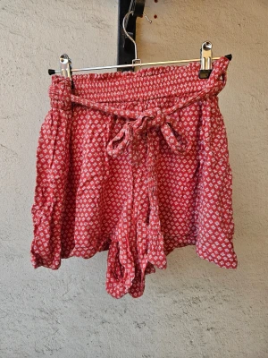 Blommiga shorts - Söta blommiga tygshorts från Primark i korallfärg med vita blommor. Modell med hög midja och skärp i midjan. Storlek 38.