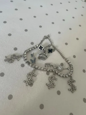 Fotlänk, örhängen & 3 st belly piercings med strass - Säljer flera smycken i silverfärg med strass: 	•	1 st fotlänk/ankelarmband med strass och dollar-hängen 	•	1 par örhängen 	•	3 st belly piercings (navelpiercingar) med olika motiv: krona, fjärilar och nyckel  Alla är dekorativa smycken i fint skick. Säljes tillsammans.