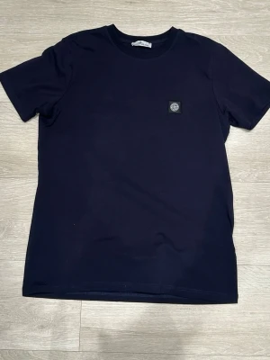 Mörkblå t-shirt från Stone Island - Snygg mörkblå t-shirt  med klassisk rund hals och korta ärmar. T-shirten har en liten logopatch på bröstet och är gjord i mjuk bomull för skön känsla. Perfekt till jeans eller shorts för en clean look. Vet inte om det är äkta eller ej så det gör de billiga priset
