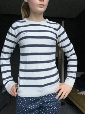 Randig stickad tröja från Hampton republic  - Säljer en vit stickad tröja från Hampton Republic med mörkblå horisontella ränder och rund halsringning. Tröjan har långa ärmar och en liten broderad logga på bröstet. Perfekt för en klassisk och avslappnad stil.