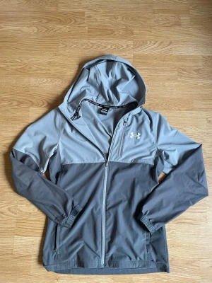 Grå vindjacka från Under Armour - Fet Under armour windbreaker. Riktigt skön och skyddar mot vinden. Inte använd så många gånger alls, så den är väldigt ny.                   Kan gå ner i pris vid snabbt köp🙌☺️