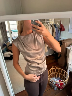 Grå/skimrig ärmlös sidenblus - Säljer en stilren grå/skimrig ärmlös blus i siden med lätt draperad front och rund halsringning. Perfekt för dig som gillar en elegant och enkel look.  💟