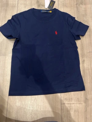 Marinblå t-shirt från Polo Ralph Lauren - Snygg marinblå t-shirt från Polo Ralph Lauren med klassisk röd logga broderad på bröstet. T-shirten har rund halsringning och korta ärmar. Tillverkad i mjuk bomull för en skön känsla och stilren look.
