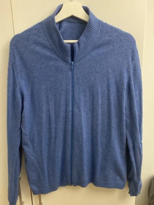 Kashmir fullzip - Mysig blå tröja med dragkedja framtill och ribbad hög krage. Tillverkad i mjukt stickat material och har långa ärmar. Perfekt för lager på lager och enkel att matcha med olika outfits.