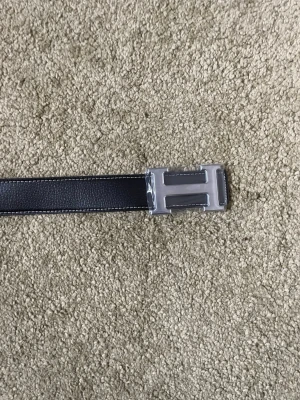 Svart bälte - Snyggt svart bälte i skinn med ett stilrent, silverfärgat H-format spänne. Perfekt accessoar för att lyfta din outfit och ge en exklusiv touch. Passar till både jeans och kostymbyxor. Bältet är 110cm långt och aldrig andvändt.