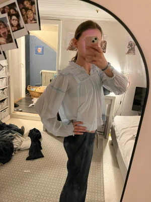 Ljusblå romantisk blus med spets - Säljer en ljusblå blus med romantiska detaljer och spetsinslag vid axlar och halsringning. Blusen har v-ringning, volangdetaljer och är tillverkad i ett tunt, luftigt material. Långärmad och perfekt för en trendig look.