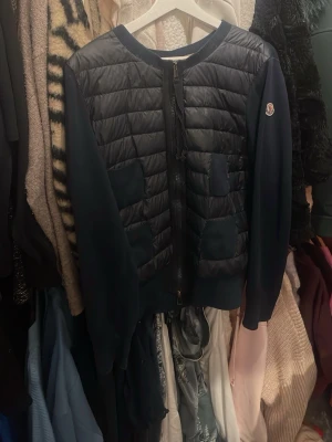 Moncler cardigan  - Snygg mörkblå cardiganjacka från Moncler fyra  fickor. Ärmar och rygg i mjukt stickat material, medan framsidan är vadderad för extra värme. Dragkedja framtill och Moncler-logga på ärmen. Perfekt för lager-på-lager. Säljer denna för att den är lite för stor och för lång, jag är en 160 och den passar bra om man gillar att ha tjockare tröjor under eller om man tycker om lite mindre tajt, jag har själv s/xs och har kunnat haft den men söker en ny och kan också gärna byta mot en cardigan i xs elr s
