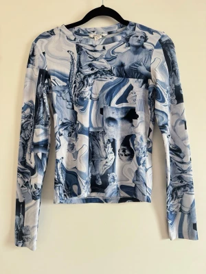 Blåvit långärmad topp med statymönster - Unik långärmad topp från Monki med blåvitt konstnärligt statymönster. Tight passform och rund halsringning. Perfekt för dig som vill sticka ut med en cool och kreativ look.