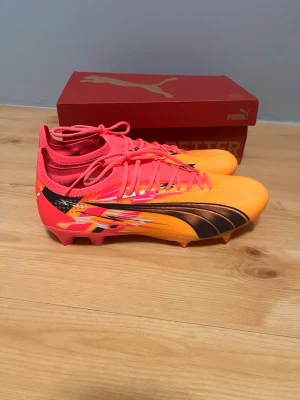 Puma Ultra fotbollsskor - Hej säljer ett par Puma Ultra Ultimate FG/AG skor | Färg sun stream-Puma Navy-Sunset glow i Christian Pulisic special edition med hans initialer där bak och spelciell limited edition | Storlek 42 och aldrig använda nypris ca 2200kr | 🧡🩷💙
