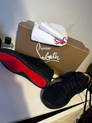 Navy  Christian Louboutin sneakers - Snygga navy sneakers från Christian Louboutin med klassisk röd sula och navy skosnören. Skorna har en låg profil och är tillverkade i mocka för en lyxig känsla. Perfekta för dig som vill sticka ut med exklusiva detaljer och ikonisk design.