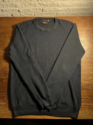 Mörkblå ribbstickad tröja Oscar Jacobson - Snygg mörkblå ribbstickad tröja från Oscar Jacobson. Tröjan har rund halsringning och är tillverkad i Italien. Perfekt för dig som gillar stilrena och klassiska plagg med en modern touch.