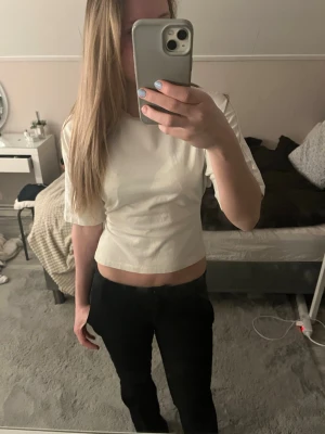 Vit croppad topp med knyt i ryggen - Säljer en vit croppad topp med korta ärmar och snygg knytning i ryggen. Toppen har en enkel och clean look, perfekt till jeans eller kjol. Materialet känns mjukt och lätt, troligen bomull eller polyester.