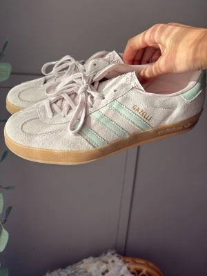 Adidas Gazelle ljusrosa/ mint gröna ränder - Snygga Adidas Gazelle sneakers i ljusrosa mocka med mintgröna detaljer. Knappt andvända. Jätte sköna. De perfekta sneakers till sommaren💚🩷