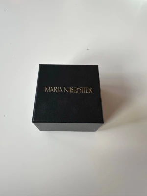 Halsband Maria Nilsdotter silverhjärta - Snyggt halsband från Maria Nilsdotter i silver med ett hjärtformat hänge och coola detaljer. Kedjan är tunn och stilren, perfekt för att lyfta din look med en unik touch. Kommer i original ask med logga. Nypris 2800kr, aldrig använd! 