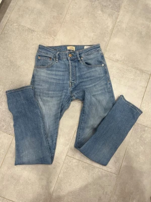 Ljusblå raka jeans från Jack N Jones  - Säljer ett par klassiska ljusblå jeans från Jack N Jones  med rak passform och fem fickor. Jeansen har knappgylf och är tillverkade i slitstark bomullsdenim. Perfekta för en avslappnad och trendig look. Riktig hög kvalitet på dessa men säljer för att de är lite för smala i midjan för mig. Använda fåtal gånger 