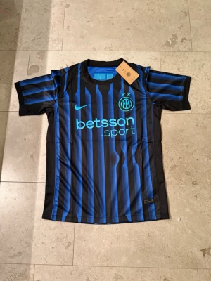 Inter Milan matchtröja Nike svart/blå - Snygg Inter Milan matchtröja från Nike i svart och blått med vertikala ränder. Tröjan har klubbmärke med två stjärnor, rund hals och sponsorlogga. Helt ny med lappar och påse.