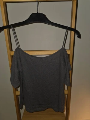 Mörkgrå axelbandslös topp - Snygg mörkgrå topp med tunna axelband och offshoulder-design. Perfekt för dig som gillar en enkel men trendig stil. Materialet känns mjukt och lätt, vilket gör den skön att bära till olika outfits.