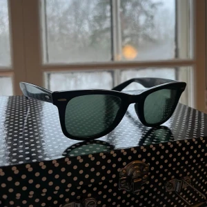 Rayban Solglasögon - Klassiska snygga svarta solglasögon med rektangulära bågar och mörka glas. Siddelarna går utåt mkt så skulle behöva spännas åt.