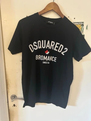 Svart Dsquared2 t-shirt Bromance - Snygg svart t-shirt från Dsquared2 med texten 'BROMANCE' och ett rött lönnlöv på bröstet. Klassisk rund hals och korta ärmar. Perfekt för dig som gillar streetwear och vill ha en stilren look med tydlig logga.