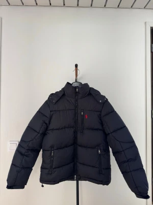 Svart pufferjacka från Ralph Lauren - Säljer en svart Polo Ralph Lauren pufferjacka storlek S. Hög krage dragkedja fram två fickor med dragkedja, röd logga på bröstet och quiltad design. Perfekt för vintern  mer info i DM.