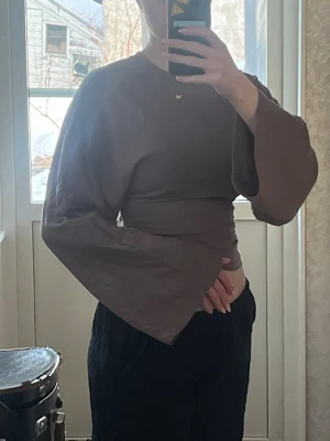 Brun topp med vida ärmar - Säljer en brun croppad topp med supervida, långa ärmar och rund hals. Toppen har en tight passform i midjan och är i ett mjukt bomullsliknande material. Perfekt för dig som gillar statement-ärmar och en unik look.