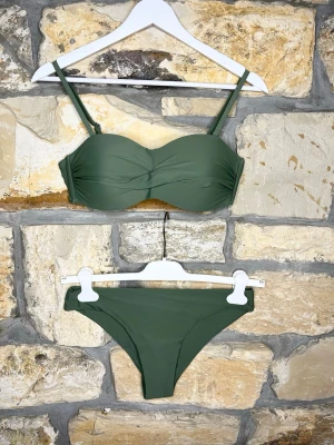 Olivgrön bikini med twistad topp - Snygg olivgrön bikini med twistad bandeau-topp och justerbara axelband. Klassiska bikinitrosor med enkel design. Perfekt för strandhäng eller poolparty. Materialet känns mjukt och följsamt mot huden.