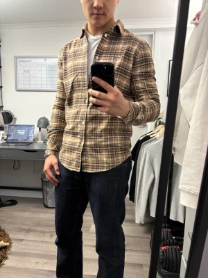 Brunrutig skjorta från Samsoe Samsoe - Säljer en brunrutig skjorta från Samsoe Samsoe med klassisk krage och vita knappar. Skjortan har långa ärmar och är tillverkad i mjuk bomull. Perfekt för en avslappnad men snygg stil.