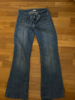Blå utsvängda jeans med fickor - Snygga blå jeans med utsvängda ben och markerade sömmar längs framsidan. 