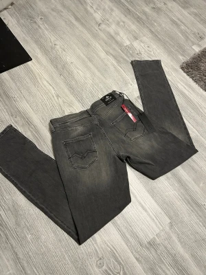 Grå slim fit jeans från replay  - Snygga grå slim fit jeans från Jack & Jones med klassisk femficksdesign och diskreta slitningar. Jeansen har raka ben och är tillverkade i mjukt denimtyg med stretch för extra komfort. Perfekta för en avslappnad och trendig look.
