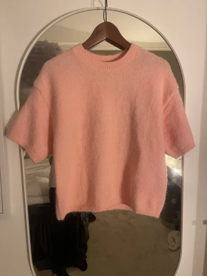 Ljusrosa stickad tröja Lindex - Supersöt ljusrosa stickad tröja från Lindex med korta ärmar och rund hals. Tröjan har en boxy, lite croppad passform och är gjord i ett mjukt, fluffigt material som känns riktigt cozy. Perfekt att styla med jeans eller kjol för en chill look. Helt ny 