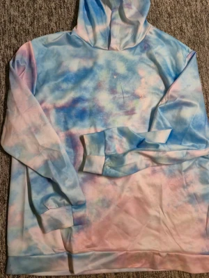 Pastellfärgad tie-dye hoodie - Säljer en oversized hoodie i mjukt material med pastellfärgat tie-dye mönster i blått, rosa och vitt. Hoodien har huva och långa ärmar med ribbade muddar. Perfekt för dig som gillar färg och vill ha en chill vibe på din outfit. STORLEK XXL, FINNS I HÄSSELBY 
